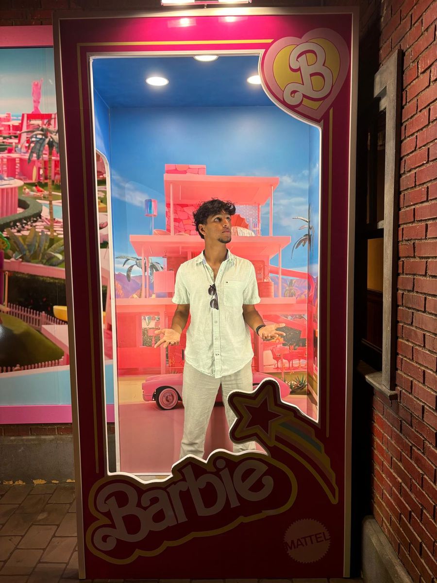 Standing inside a life-size Barbie box display outside a brick building.
