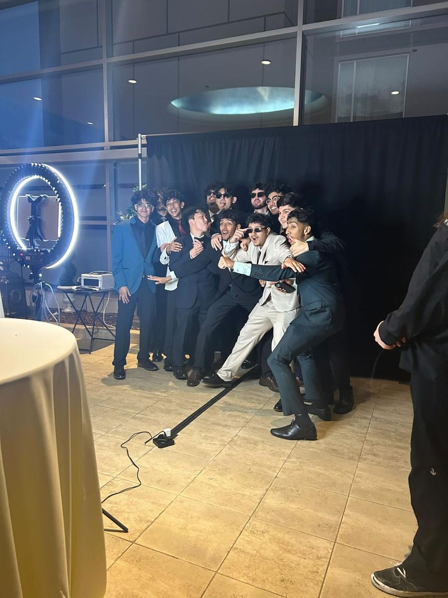 A large group piled together in front of a ring light for a photo booth shot at a formal event.