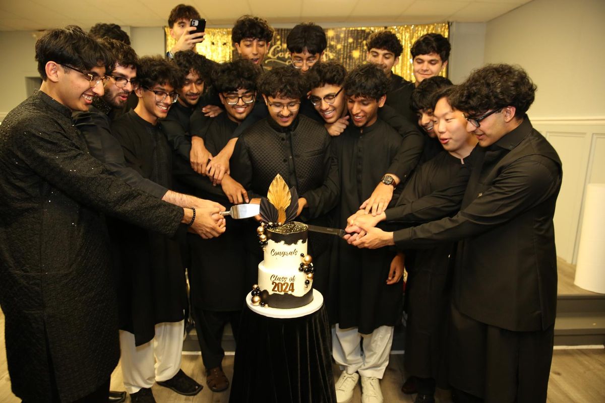 A group in matching black kurtas cutting a Class of 2024 cake together.
