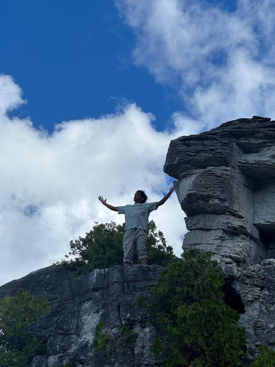 Standing on a limestone outcrop with both arms out, cloud and blue sky behind.