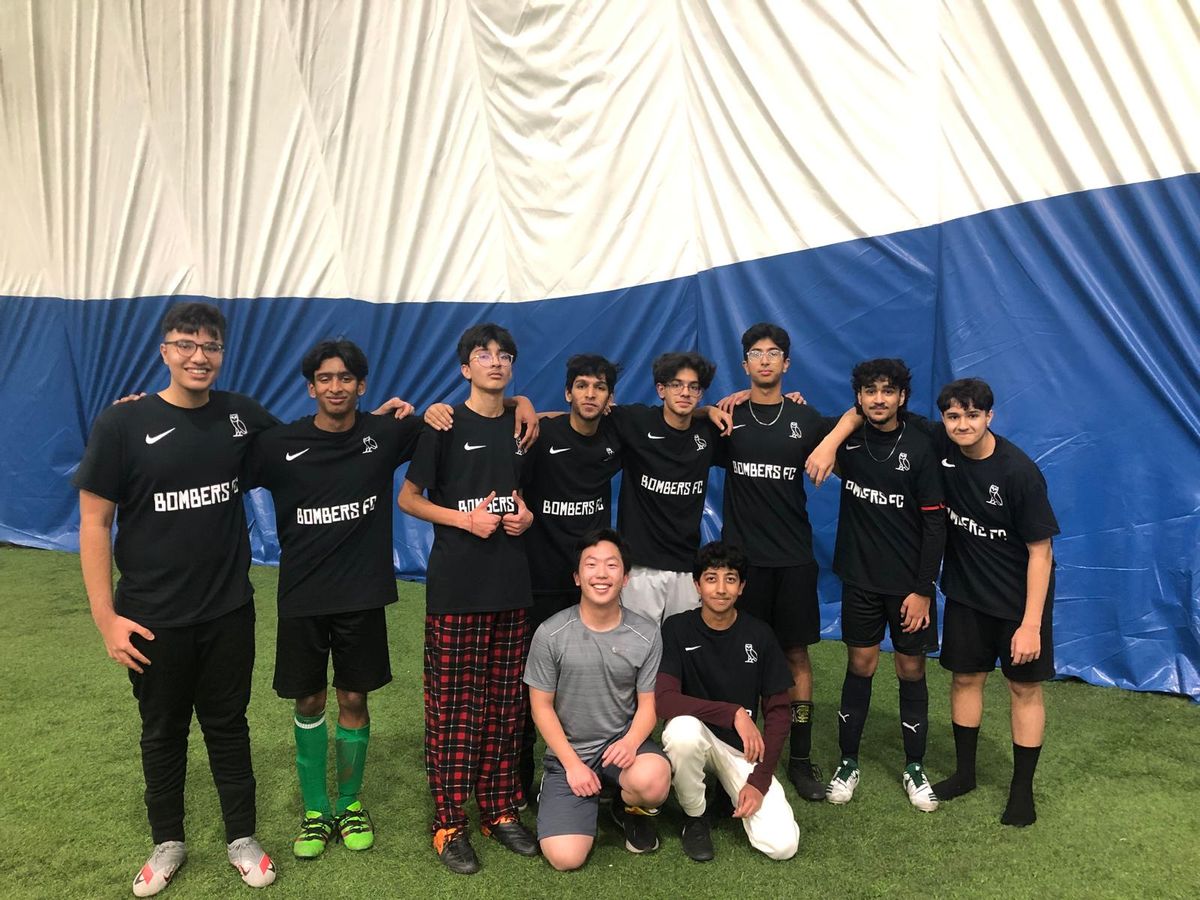 A soccer team in black jerseys lined up on an indoor turf pitch for a team photo.