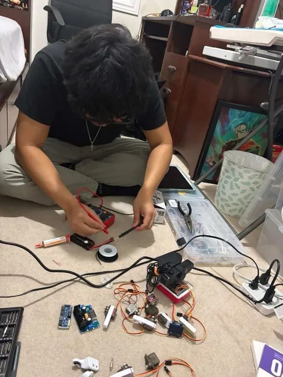 Probing a component with a multimeter on the floor, servos and driver boards spread out alongside.