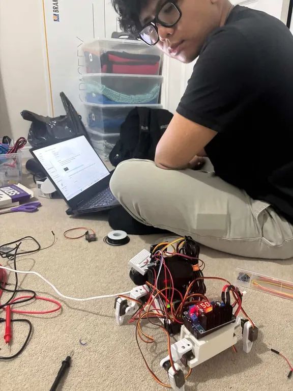 Sitting on the floor beside the half-assembled robot, laptop open, wiring spread across the carpet.