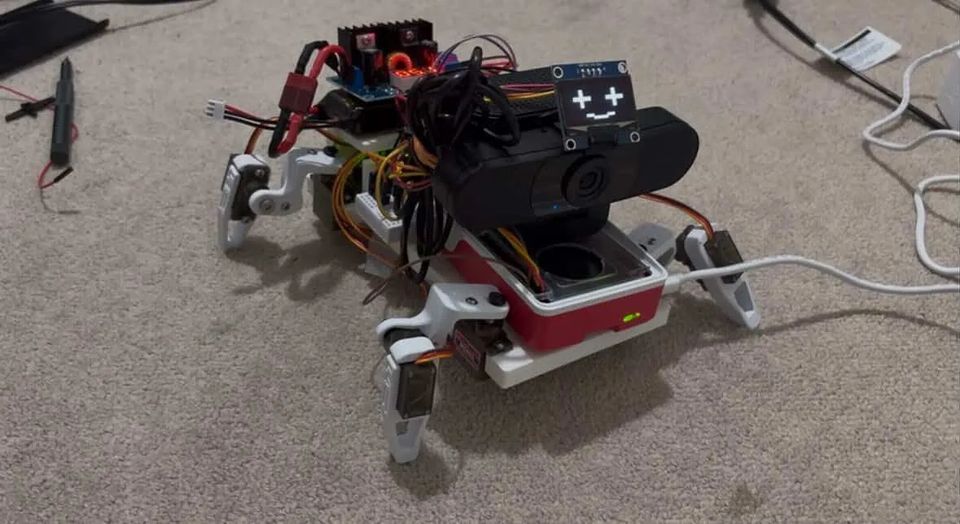 The robot on the carpet with all four legs attached and the OLED face lit.