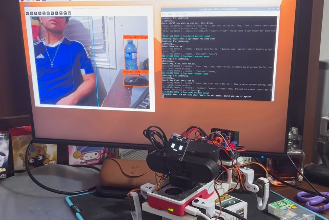 A monitor showing the annotated camera feed with detection boxes around a person and a bottle, beside a terminal window logging the conversation, with the robot on the desk below.