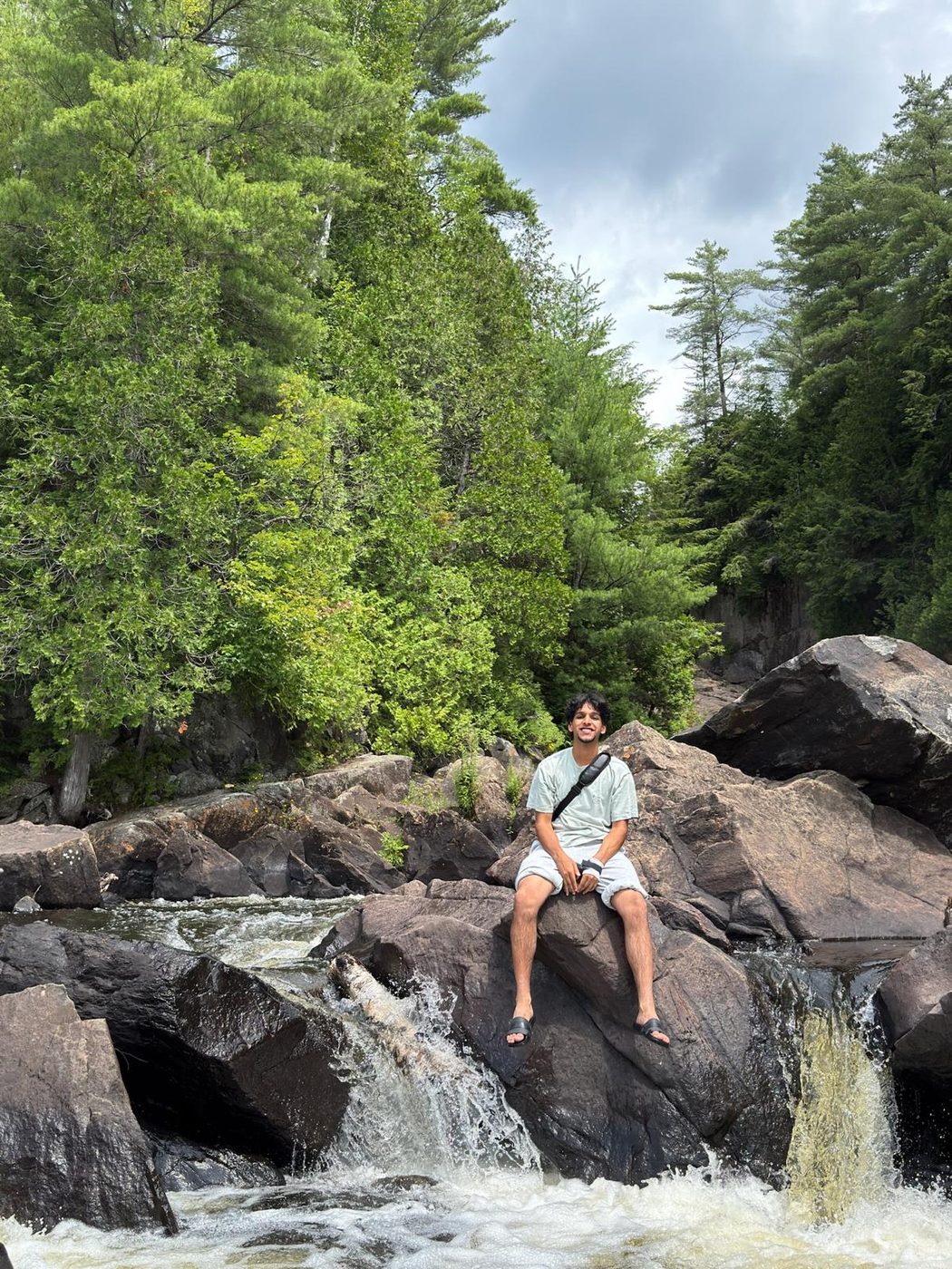 Sitting on a rock beside a waterfall running through a wooded gorge at the end of a hike.