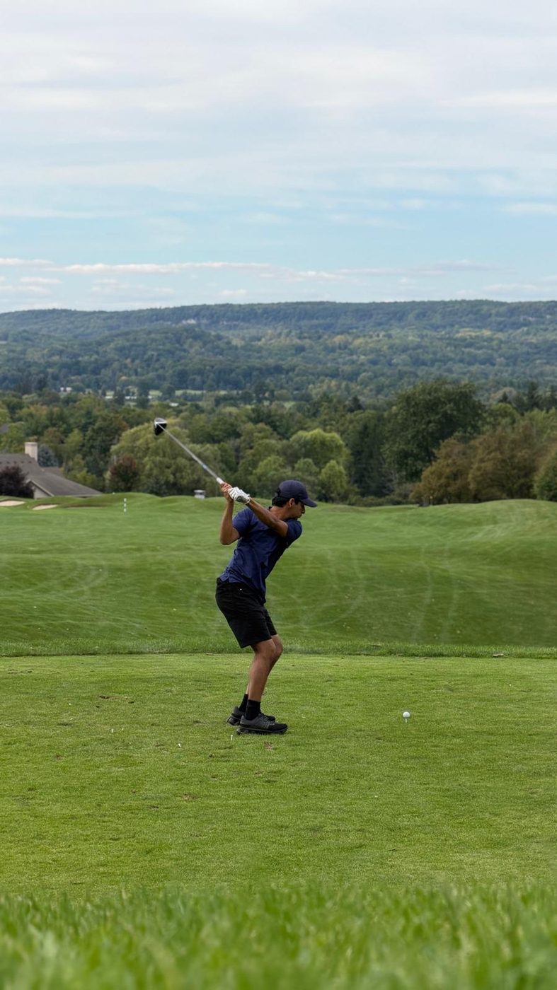 Mid follow-through on a tee shot, looking down a wide fairway toward a treeline.