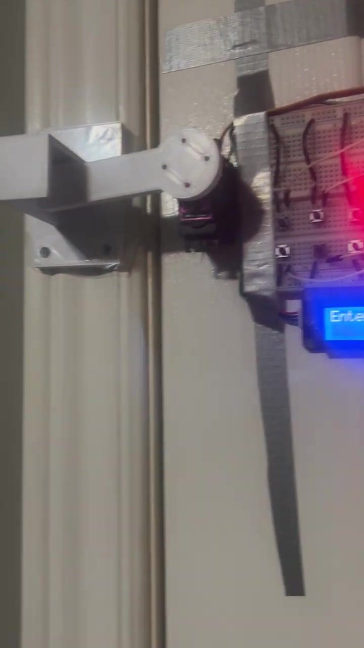 The servo arm lying flat against the door frame, holding the latch closed, with the LCD lit below.